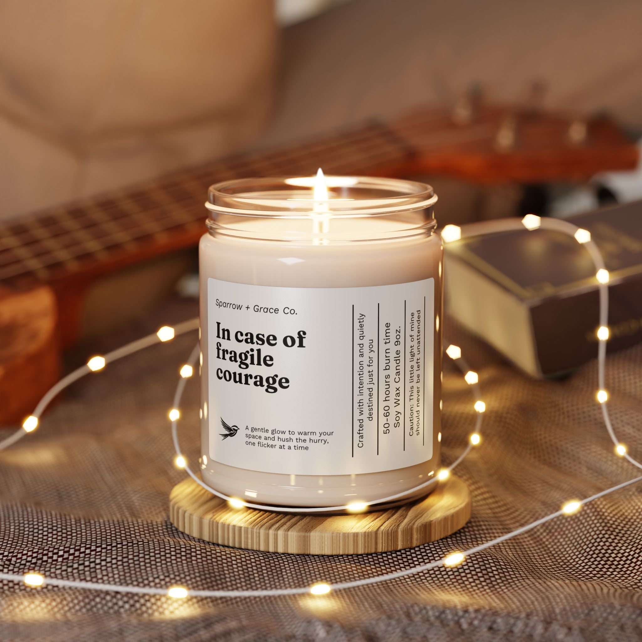 Candle in a jar with a label on a wooden coaster surrounded by string lights and a guitar in the background