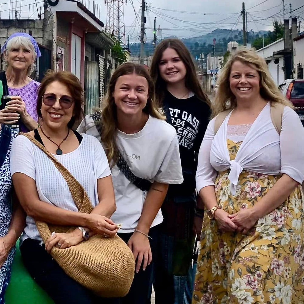 Group of women posing in front of a large green letter 'H' on a street.
