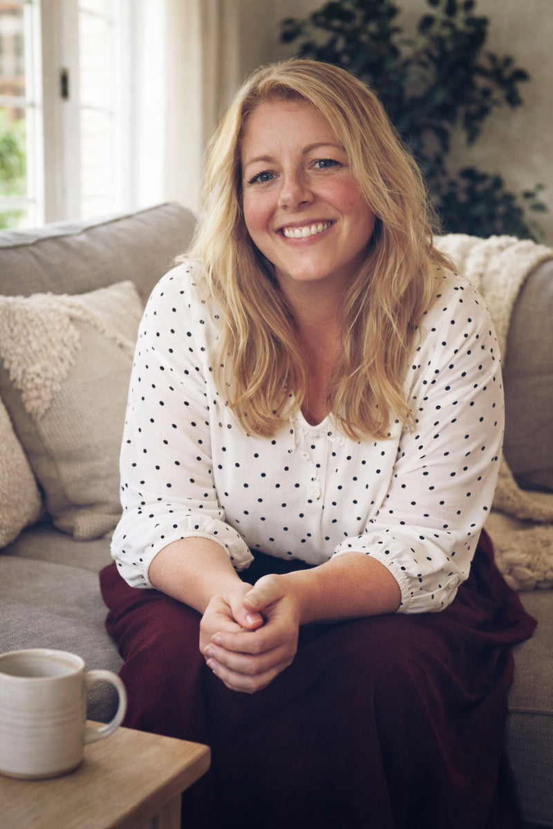 Woman sitting on a couch with a cup of coffee, smiling.