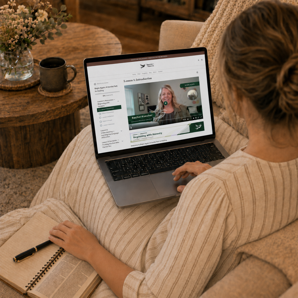 A woman sits on a beige couch in a cozy living room, viewed from behind, using a laptop to watch a video course. She is wearing a beige ribbed sweater and has an open notebook and pen on her lap.