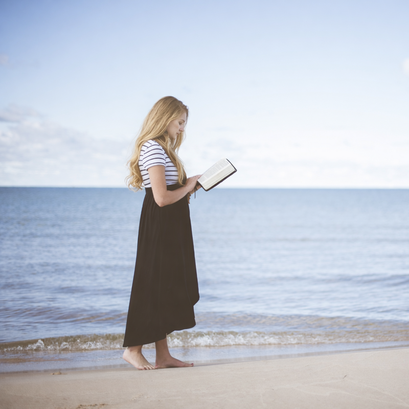 Woman standing on a beach holding a book with ocean and sky in the background