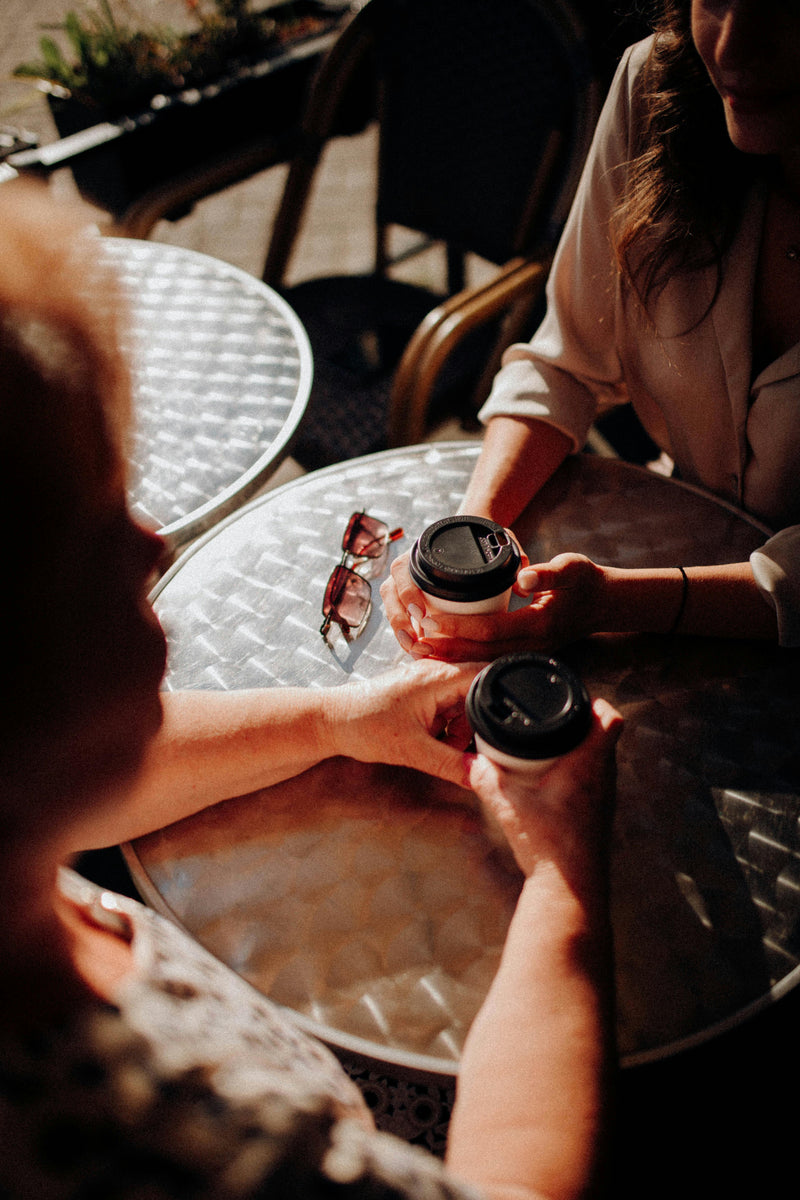 Two people holding coffee cups at a table outdoors
